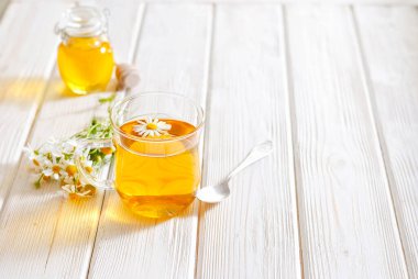 Papatya çiçekli bir fincan bitki çayı ve beyaz ahşap arka planda bal. Fotokopi alanı ile doğal organik alternatif tıp konsepti. Günaydın güneşli sabah.