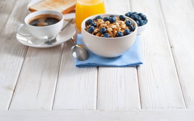 Granola ve yaban mersinli kahve ve pişmiş tost. Fotokopi alanı olan beyaz ahşap masada lezzetli bir kahvaltı. Sabahları sağlıklı ve lezzetli yiyecekler yulaf ezmeli fındıklı ve meyveli böğürtlenli