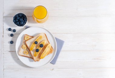 Muz ve portakal suyu ile yabanmersinli kahvaltı ve beyaz ahşap masa üzerinde pişmiş tost fotokopi alanı ile yatıyordu. Sabahları yulaf ezmeli sağlıklı yiyecekler.
