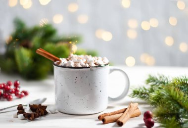 Noel beyaz bardağı sıcak çikolata ve marşmelov ve tarçın çubuklarıyla kırmızı böğürtlen ve güzel çelenk ışıklarıyla köknar ağacı dalları. Yeni yıl kutlaması