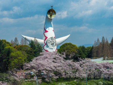 JAPAN, OSAKA - APRIL 13, 2017: Cherry Blossums in front of the Tower of the sun which an existing exhibit from the World Expo in 1970 clipart