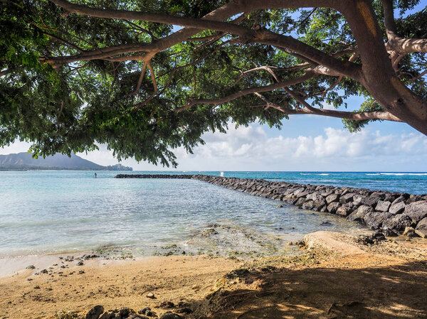 USA, HAWAII - AUGUST 30, 2018: Breakwater leads out into the ocean from the the shade of tree on the beach in Hawaii