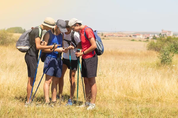 young people with trekking poles doing the Way of Saint James in Spain seeing on their mobile phone the selfie photograph they have taken when they arrived at the destination village on a summer day