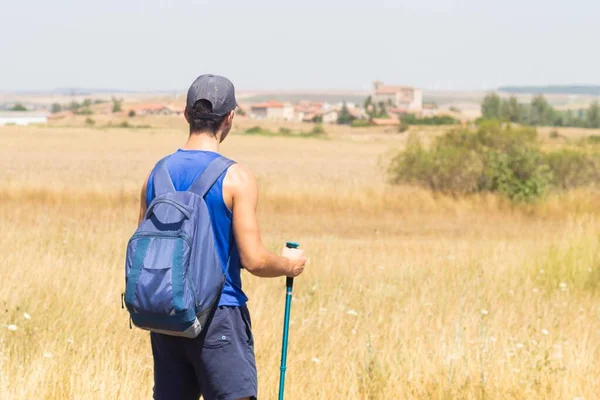 Sırt çantalı ve sopalı genç adam yaz günü İspanya 'da Camino de Santiago' yu yapan Atapuerca köyüne bakıyor.