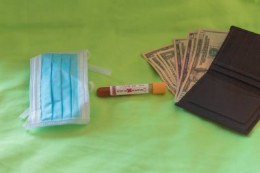 Covid19 'a karşı yapılan hijyenik maske testi pozitif sonuç veriyor ve diğer tarafta yeşil arka plan konsepti üzerine para koruma satın alma ve seçici odaklanma.