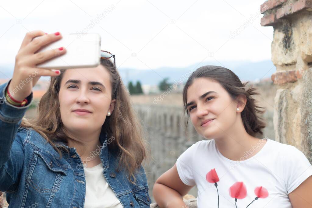 two young teenagers taking a selfie photograph with the monument of the aqueduct of Segovia in Spain as background in a summer day