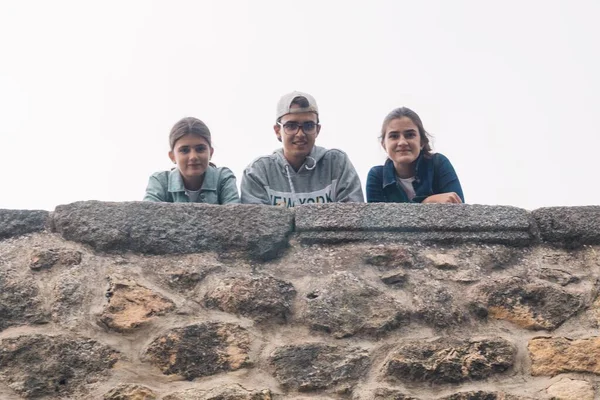 2人の少女と若い10代の若者が曇った日に石の壁から笑顔で見下ろし — ストック写真