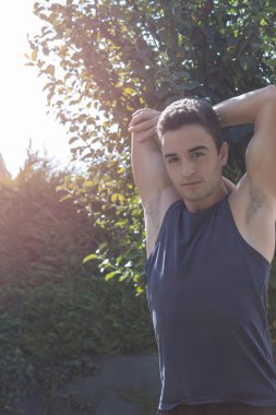 Spor elbiseli genç bir çocuğun kollarını ve omuzlarını esneterek güneşli bir günde evin bahçesinde spor egzersizleri yapmaya başlaması.