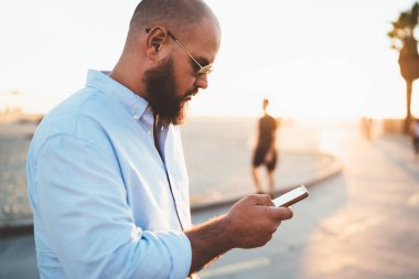 Dalgın sakallı adam akıllı telefon hücresel açık havada duran üzerinden sosyal ağlar bloglama içerik yükleme sokak, erkek hipster üzerinde iyi bir internet bağlantısı üzerinden uygulama yükleme