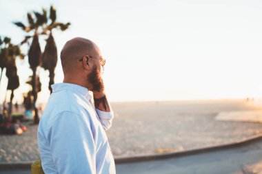 Genç hipster adam görünümlü dış görev seslenmek yolu ile smartphone ile arkadaş açık havada, yakışıklı erkek gezici telefon konuşmayı konuşurken bağlantı ve cep telefonu ile memnun tarifeler