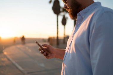 Hipster adam modern cep telefonu elinde göz web sayfasından, genç adam 4 g internet bağlantısı açık havada duran kullanarak Smartphone'da kısa mesaj gönderme haber okuma görünümünü kırpılmış