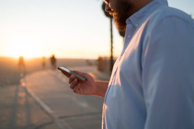 Genç adam online şehir sokak, hipster adam pay fotoğraf blog yolu ile uygulama açık havada süre sosyal ağlar posta kontrol üzerinde ayakta rezervasyon yapmak için smartphone kullanarak görünümünü kırpılmış