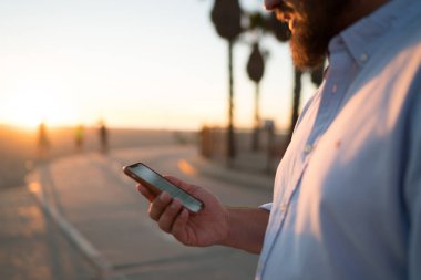 Sakallı erkek holding cep telefonu haber bilgi göz web sayfası ayakta Caddesi üzerinde okuma, Resim kırpılmış, hipster adam görüş fotoğraf içinde sosyal ağlar bloglama online yolu ile smartphone