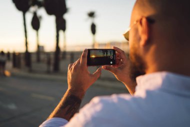 Gün batımı sırasında tatil, modern smartphone ve uygulama alarak resim Doğa gezisi sırasında kullanılarak hipster adam güzel manzara çekim için erkek holding cep telefonunuzun arka görünümü kadar kapatın