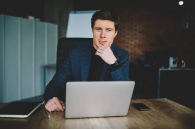 Yarım uzunluk portre müreffeh şirket sahibinin kabine modern dizüstü bilgisayar için ağ, kendine güvenen işadamı kamera üzerinde çalışma yer netbook kullanarak vakit bakarak yakın oturan