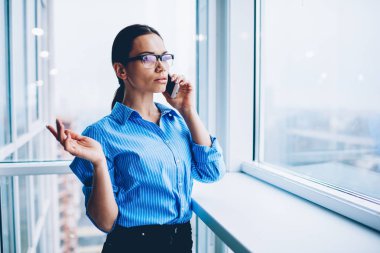 Office, ciddi kadın Yöneticisi denetimi para denge için bankacılık işlecini çağırmak coworking ayakta ucuz telefon tarifeleri kullanarak ortağı ile telefonda konuşurken Eyewear emin iş kadını