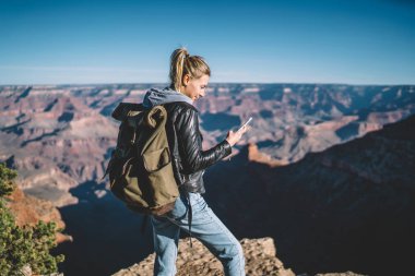 Gülümseyen kadın Amerikalı turist smartphone cep telefonu ile iyi veri bağlantısında dağlar, sırt çantası elinde vahşi doğa'da cliff yürüyüş üzerinde duran cep bakarak kadınla memnun mesajı okumak