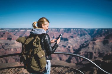 Dağlarda, pozitif kadın Gezgin vahşi doğa keşfetmek akıllı ileti gönderme turistik güzergah üzerinde hiking iyi mobil bağlantı kontrol sırt çantası ile genç hippi kız avare gülümseyen