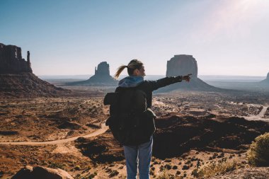Arkadan Görünüm Monument Valley güzel manzara kumtaşı oluşumu ile işaret eden sırt çantası ile genç kadın Gezgin, hippi Kız Navajo rezervasyonu hiking sırt çantası ile keşfetmek benzersiz Jeoloji