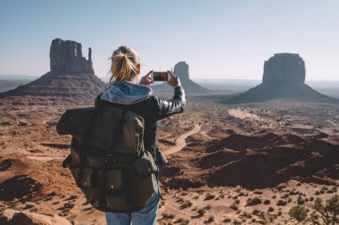 Monument Valley smartphone kamera, resim yapma ABD doğasını keşfetmek kumtaşı oluşumu telefonla hippi kız ile manzara manzara fotoğrafçılığı sırt çantası ile arkadan görünüşü erkek