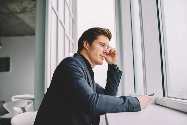 Dreamy prosperous businessman looking at window in loft interior office thinking about future plans,contemplative male entrepreneur enjoying leisure on work break concentrated on idea for rest