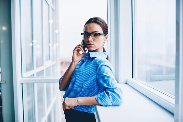 Portrait of confident female economist checking banking account of corporation having mobile phone consultancy with operator,serious businesswoman having telephone conversation looking at camera