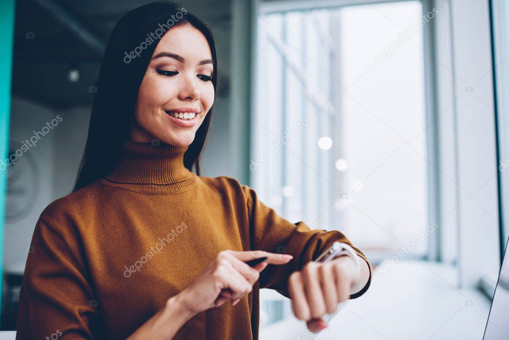 Smiling asian businesswoman checking time and notification of new message on modern wearable computer,prosperous female entrepreneur satisfied with advanced gadget for communication and organizing