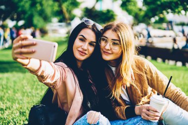 Smartphone uygulama kullanarak akıllı güzel resim yapma neşeli arkadaşlar. Çekici genç kadın üzerinde modern telefon açık havada hafta sonu serbest zaman sırasında poz selfie yapma