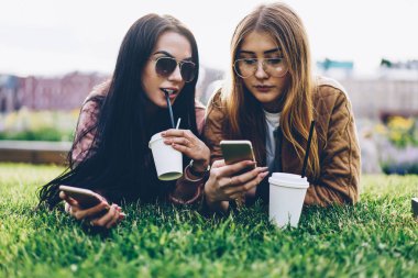 Central Park'ta çim üzerinde yalan ve sosyal ağlar üzerinde akıllı telefonlar kolay sohbet mesajlaşma süre alanını sahte ile lezzetli kahve içecek içme şık Güneş gözlükleri çekici genç kadın