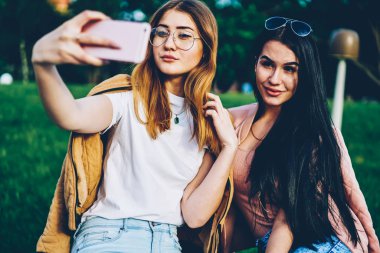 Çekici genç kadın selfie fotoğrafları smartphone harcama yapma şık güneş gözlüğü ile birlikte parkta serbest zaman. Arkadaşlar kendi blogunuzda yayımlamak için dijital cep telefonunda fotoğraf çekmek
