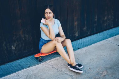 Radyo earphones favori müzik durulması esmer genç kadının modern smartphone-e doğru açık havada kaykay üzerinde otururken bağlı. Sevimli bayan patenci dinleme şarkıları