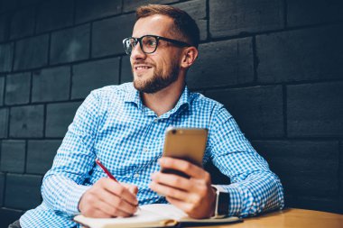 Kafe, uzağa arıyorsunuz smartphone üzerinden Web sitesinde online rezervasyon sırasında notlar yapma işadamı yaratıcı çalışma ile profesyonel erkek mimar not defterinde grafik çizim Eyewear memnun