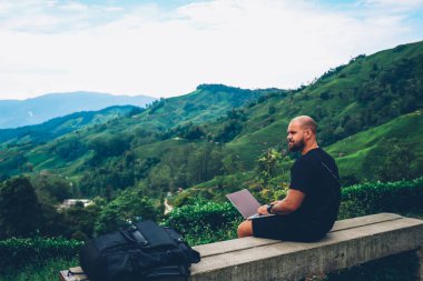 Düşünceli genç sakallı adam mesafesi iş modern bilgisayar kablosuz 4 g için bağlı sırasında çalışma çözüm üzerinde düşünme yüksek dağlarda oturan ve yeşil doğal çevre zevk internet