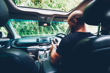 Kiralık Araba dümene oturan navigator yüklemek için pano Smartphone bağlanma genç adam Gezgin sakallı. Turizm medya yolda durdurmak sırasında dijital telefon üzerinde dosyaları eşitler