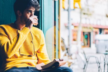 Yaratıcı genç adam ise pencereden dışarı bakıyor ve zamanlama oluşturmak için yeni fikirler üzerinde düşünme lezzetli kahve içme sakallı. Düşünceli erkek içecek keyfini rahat sarı Kazak giymiş