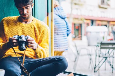 Sakallı erkek profesyonel fotoğrafçı filtreleri vintage fotoğraf makinesinde seçme ve kahve dükkanında istirahat ederken fotoğrafları izlerken ekran pencere iç ayar yapma rahat kıyafet giymiş