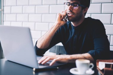 Kırpılmış görüntü optik gözlük dizüstü bilgisayar başında oturan müşteri ile smartphone üzerinde konuşmak için Kablosuz 4 g bağlıyken muhasebe raporları kontrol dalgın grafik tasarımcı internet