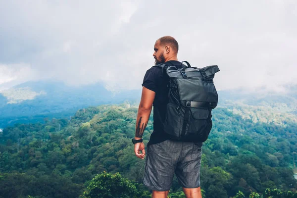 Tepenin üstünde duran ve Asya manzaralar keşfetmek yaz trek sırasında gri bulutlar ile kaplı yeşil saç ekimi ile dağlar güzelliği zevk siyah sırt çantası ile arkadan görünüşü erkek uzun yürüyüşe çıkan kimse