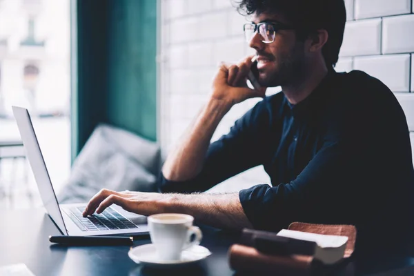 快乐男性企业家的侧面视图现代笔记本电脑键盘上的眼镜打字在搜索信息时 与朋友坐在咖啡馆里聊天 — 图库照片