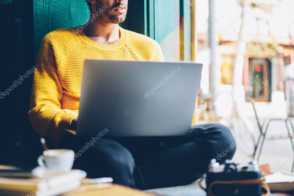 Cropped image of male graphic designer looking out of window while working freelance at laptop computer connected to wireless internet.Thoughtful copywriter doing distance job at netbook in coworking