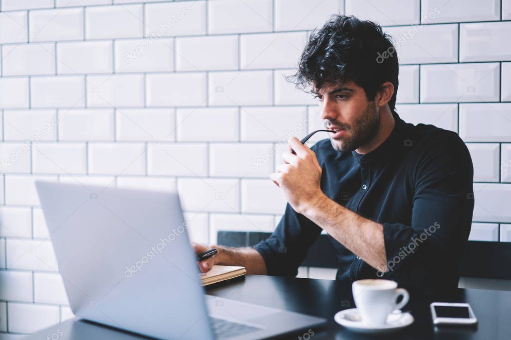 Concentrated male graphic designer watching carefully online lesson on laptop computer connected to 4G internet.Pensive entrepreneur checking accounting database on netbook working in coffee shop