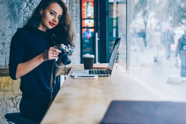 Kablosuz internet'e bağlanan dizüstü bilgisayar oturan vintage fotoğraf makinesi ayarlarını yaparken kameraya bakıyor güzel kadın fotoğrafçı portresi. Kopyalama alanı alanı reklam için
