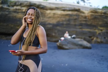 Smartphone ayakta deniz kenarı bağlı kulaklık serin ses şarkıları zevk dreads ile mutlu afro Amerikan atlet. Eğitim müzik dinleme için etkin giysili jogger olumlu koyu derili