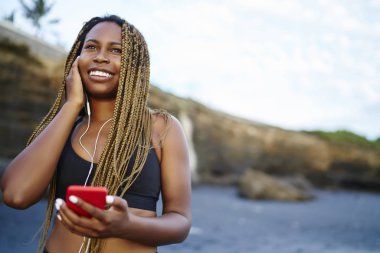 Spor üst modern kulaklık smartphone için spor egzersiz duran tropikal Adası Deniz coasline bağlı favoutite müzik şarkıları dinlerken neşeli afro Amerikan kadın atlet giymiş