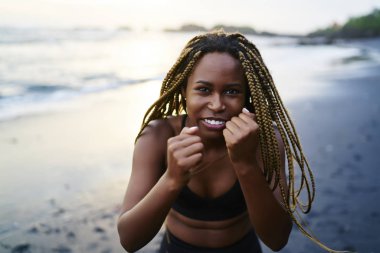 Yarım uzunluk portre ile konsantre siyah sportif kızın sabah egzersiz sırasında eğitim egzersizleri yaparken kameraya bakarak ödü kopar. Afro Amerikan erkek boks sahil üzerinde çalışmaktadır