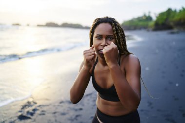 Sabah spor kameraya bakarken deniz kıyı şeridi üzerinde eğitim sırasında el şeklini geliştirmek için afro Amerikan sportif kız etkin aşınma ve boks egzersizleri yapma dreads portresi yarım uzunluk