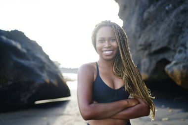 Spor sırasında çapraz eller önde kamera gülümseyen neşeli afro Amerikalı genç kadın sevgilisi portresi. Sabah sahil üzerinde egzersiz duran için etkin üst pozitif kadın jogger giymiş