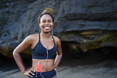 Mutlu afro Amerikalı genç kadın kamera litening ses kulaklık uygulamada müzik şarkıları ise gülüp portresi. Kameraya gülümseyen spor top neşeli koyu tenli jogger giymiş