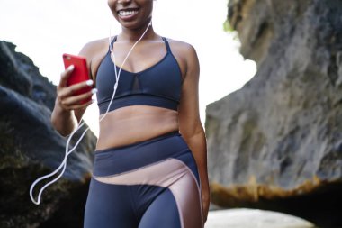 Afro Amerikan kadın jogger kulaklık olarak çalışma için müzik dinleme cep için bağlı eğitim için şık spor elbise giymiş görüntü kırpılmış. Etkin aşınmaya telefon ile yürüyüş sportif kız