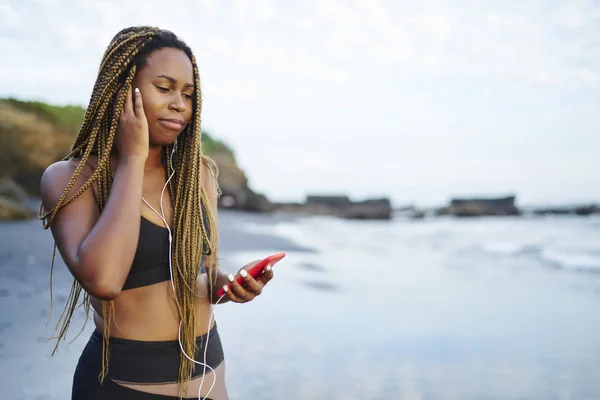 Молода Жінка Темною Шкірою Слухає Музику Навушниках Підключених Смартфона Стоїть — стокове фото